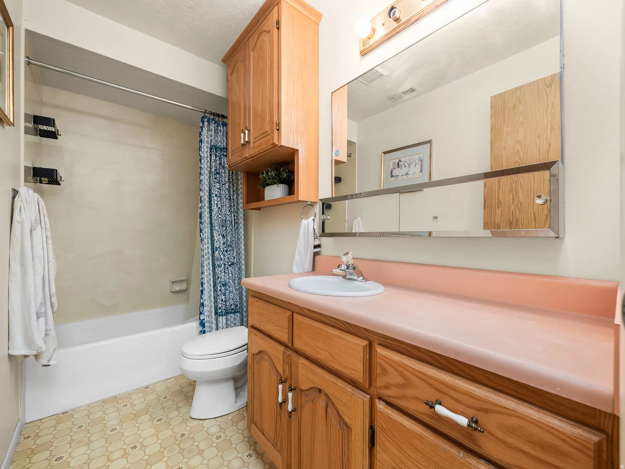 Bathroom featuring a white bathtub, toilet, wood-finish vanity with a single sink, pink countertop, and a large wall-mounted mirror