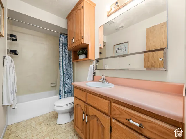Bathroom featuring a white bathtub, toilet, wood-finish vanity with a single sink, pink countertop, and a large wall-mounted mirror