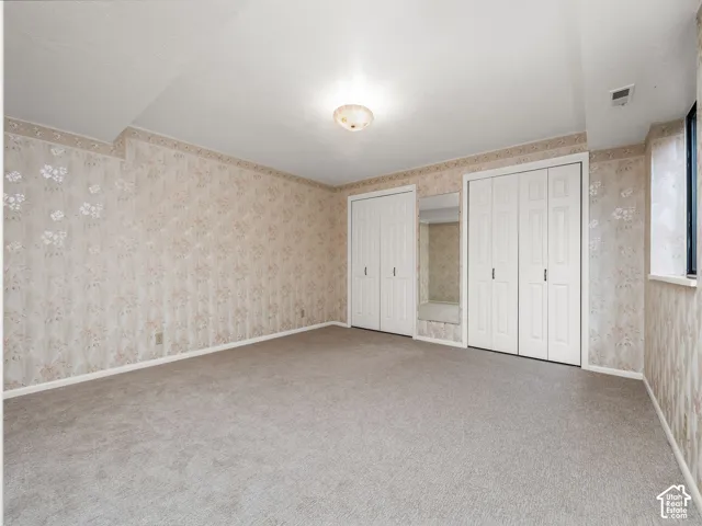 Carpeted room featuring floral wallpaper, white bi-fold closet doors, and built-in mirror