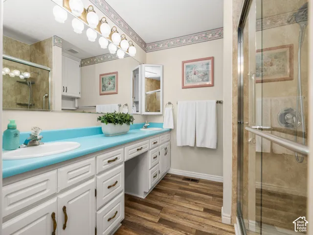 Double vanity with integrated sinks, white cabinetry, wood-finish flooring, and a glass-enclosed shower