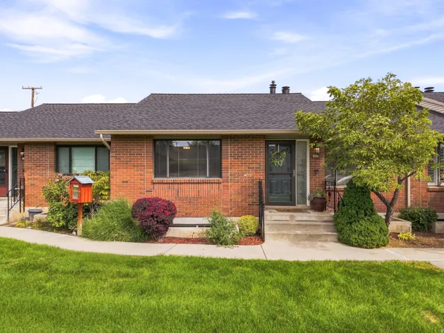 Red brick exterior with a dark shingle roof, concrete porch, and a dark entry door