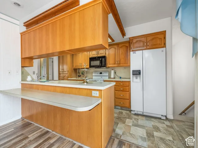 Kitchen featuring wood-finish cabinetry, built-in microwave, white side-by-side refrigerator, and a breakfast bar