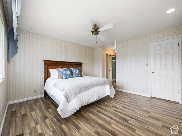 Wood-finish flooring throughout, ceiling fan with light fixture, and a solid wood headboard