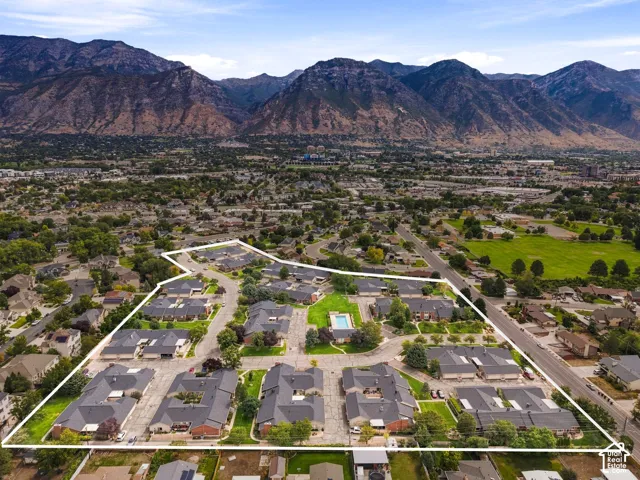 Mountain backdrop, residential development with multiple buildings, paved roads, central community pool, and surrounding green spaces