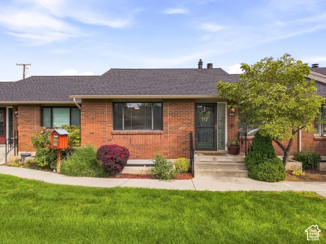 Red brick exterior with a dark shingle roof, concrete porch, and a dark entry door