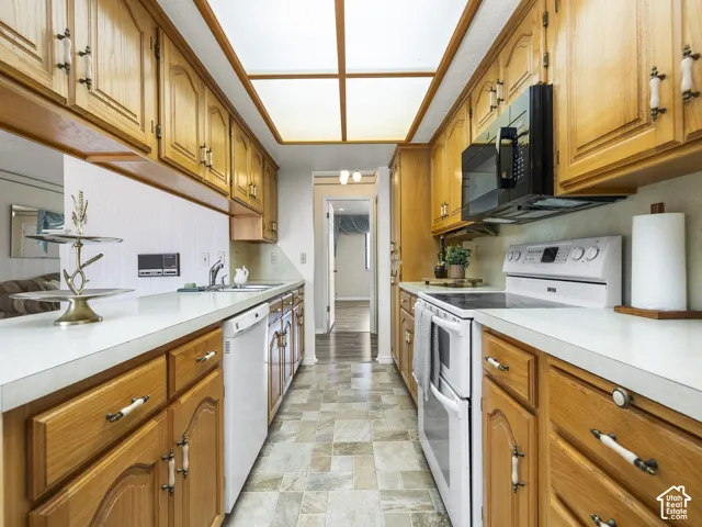 Galley kitchen featuring wood cabinetry, white countertops, built-in microwave, and oven with cooktop