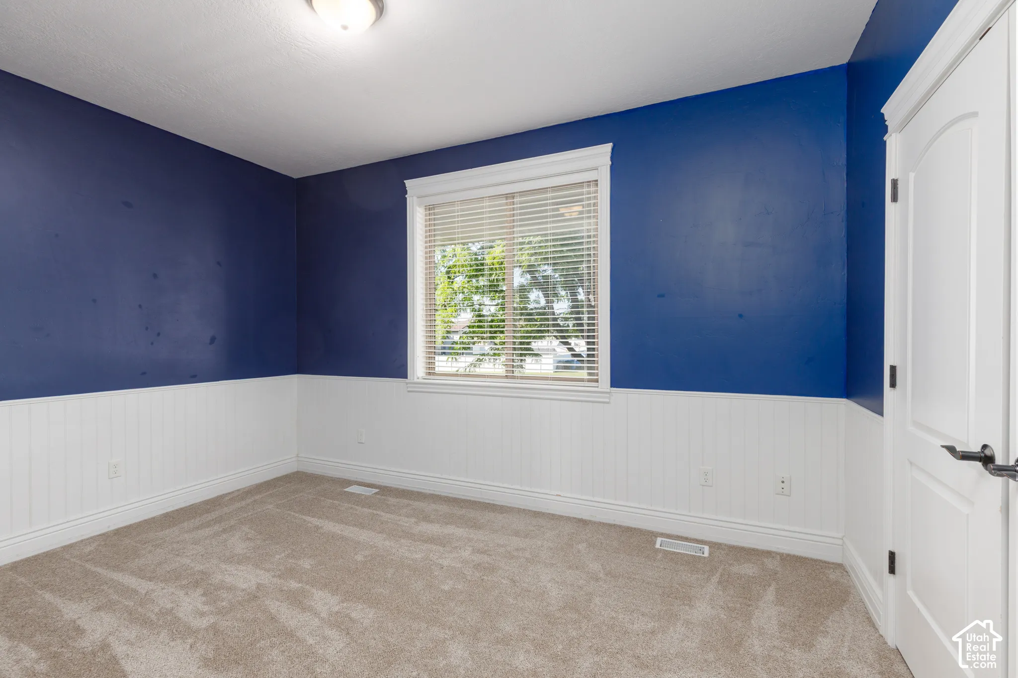 Wall-to-wall carpeting, window with blinds, beadboard wainscoting, and a panel door with dark hardware