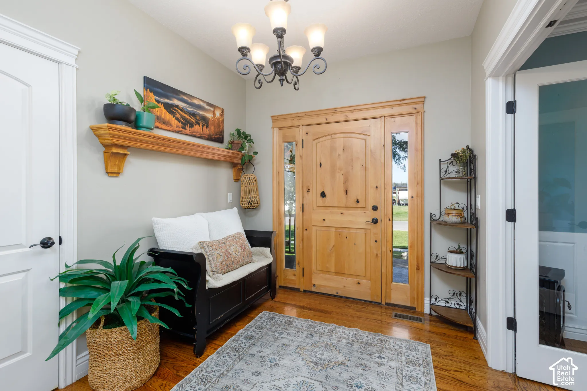 Hardwood flooring, natural wood-finish entry door with sidelights, decorative wall shelf, and chandelier with alabaster-style shades