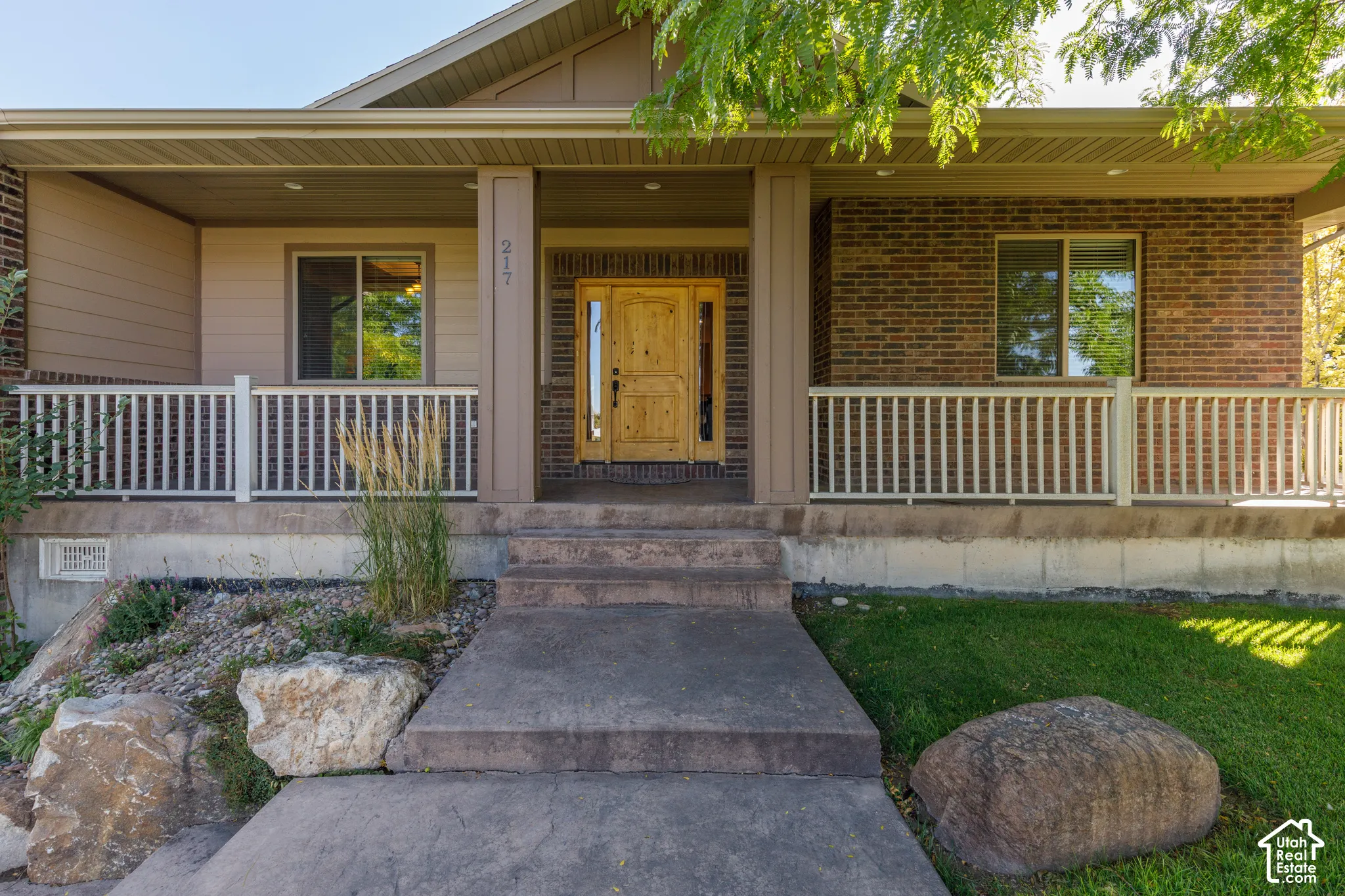 Covered front porch with a wood entry door, brick and siding exterior, concrete steps, and a concrete walkway