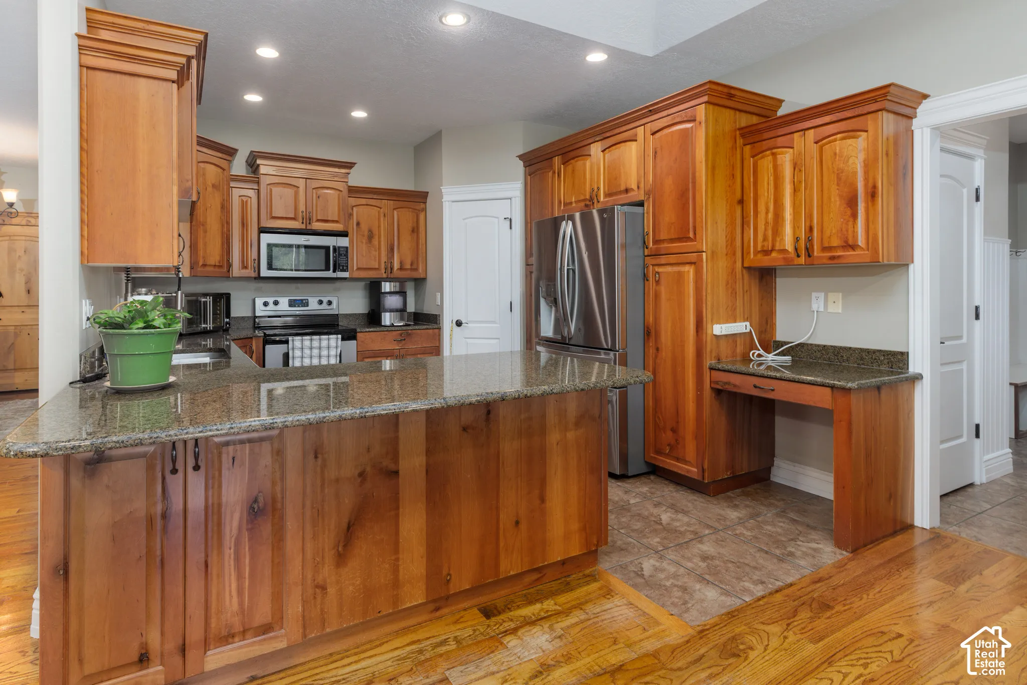 Kitchen featuring wood-finish cabinetry, granite countertops, stainless steel appliances, and a built-in desk area