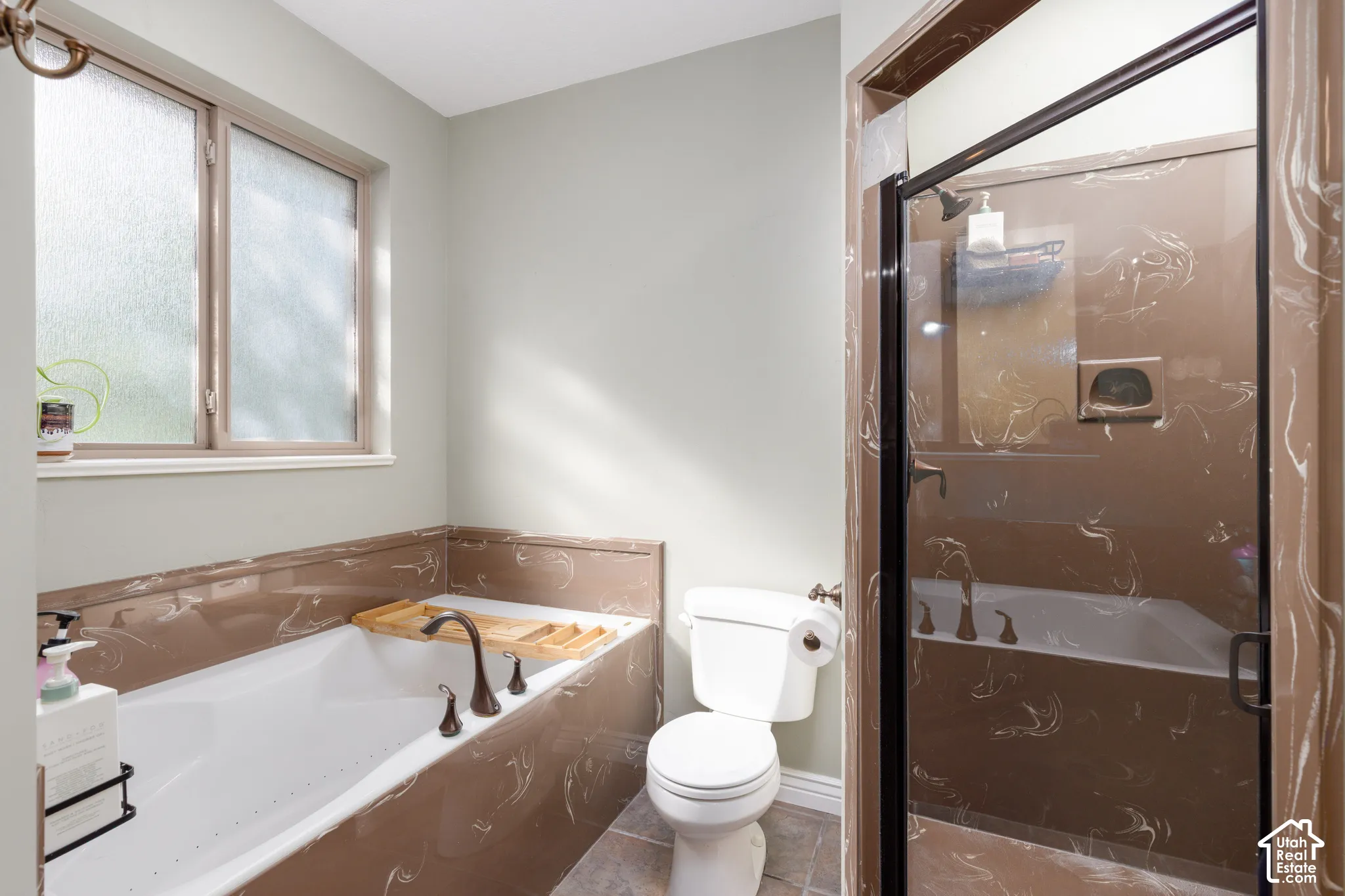 Porcelain bathtub with bronze-finish fixtures, a frosted window, and a shower with a clear glass enclosure and bronze-finish trim