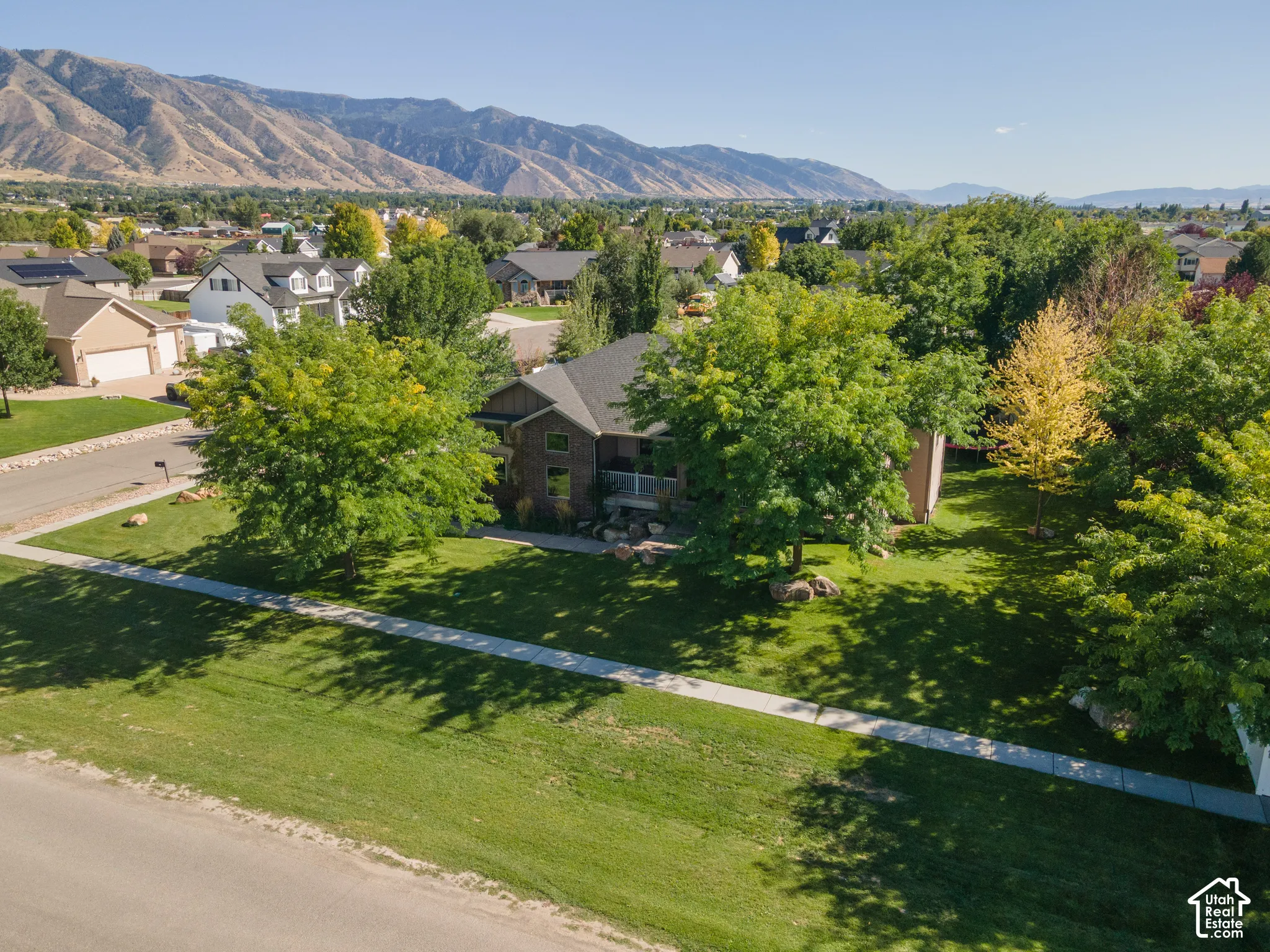 Manicured lawn, mature trees, residential neighborhood, mountainous backdrop, and a paved street