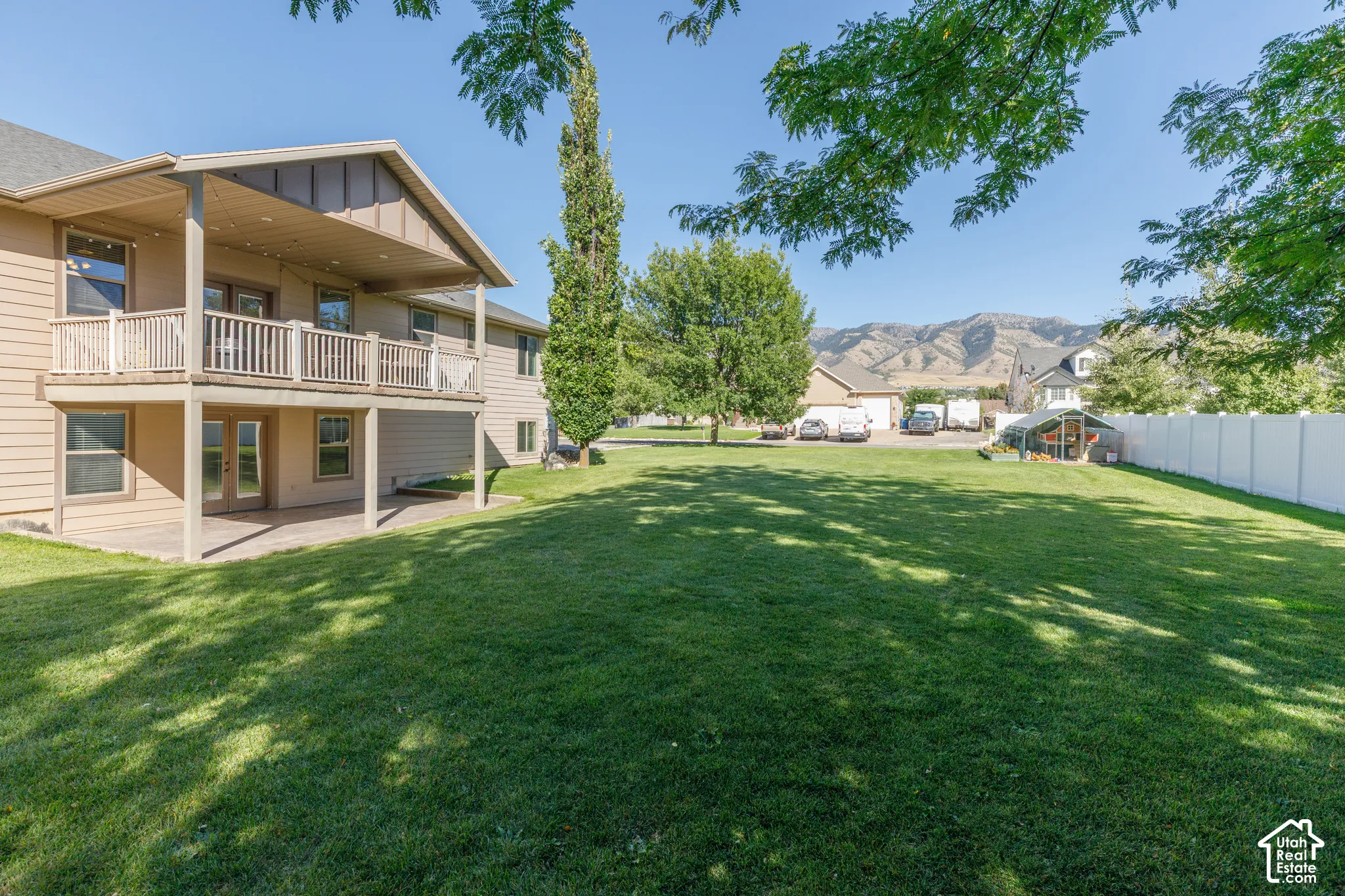 Expansive backyard with a manicured lawn, a two-story exterior featuring an upper deck and lower patio, and a mountain range backdrop