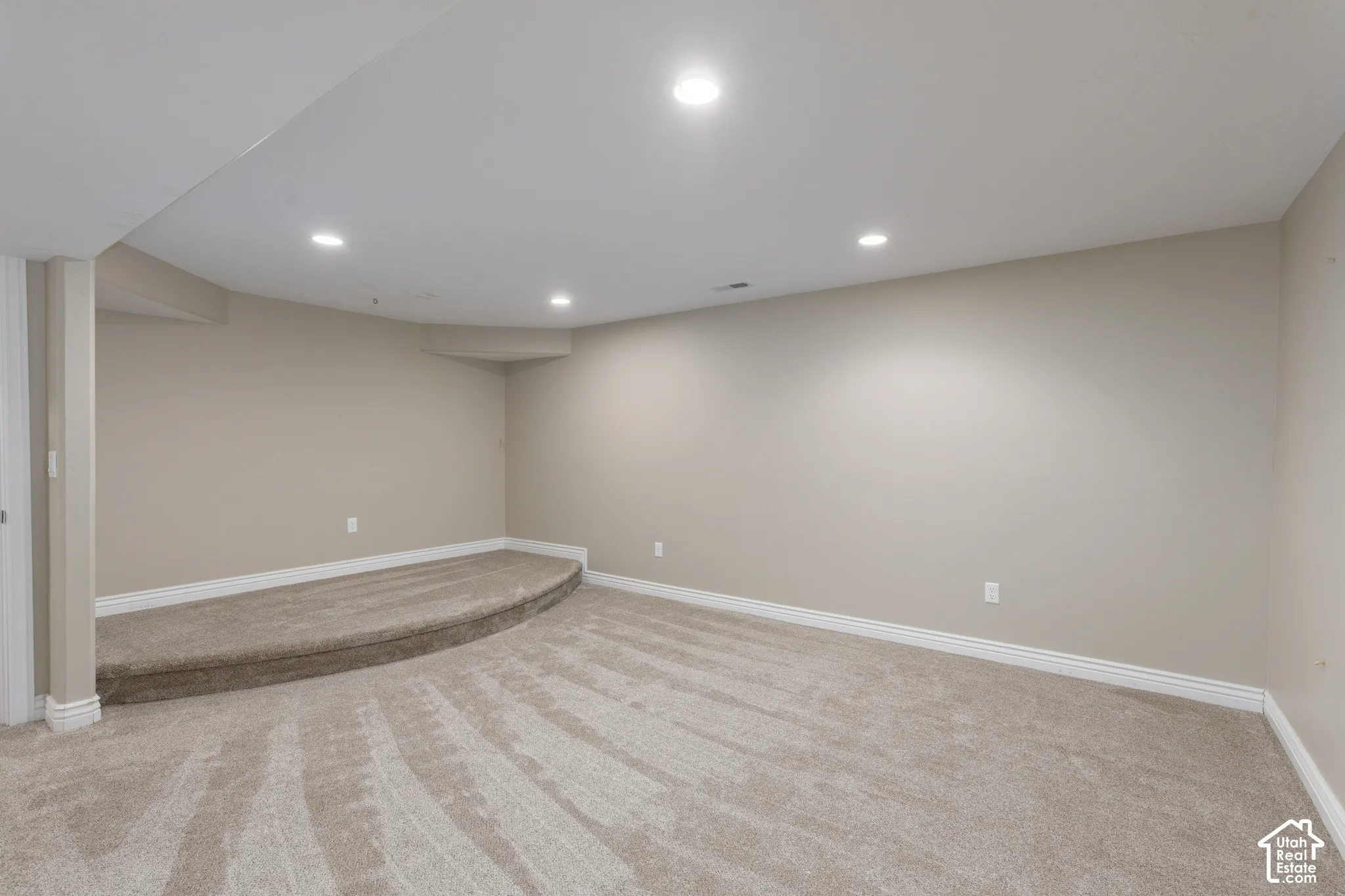 Recessed lighting illuminating a spacious room with wall-to-wall carpeting and a raised carpeted platform