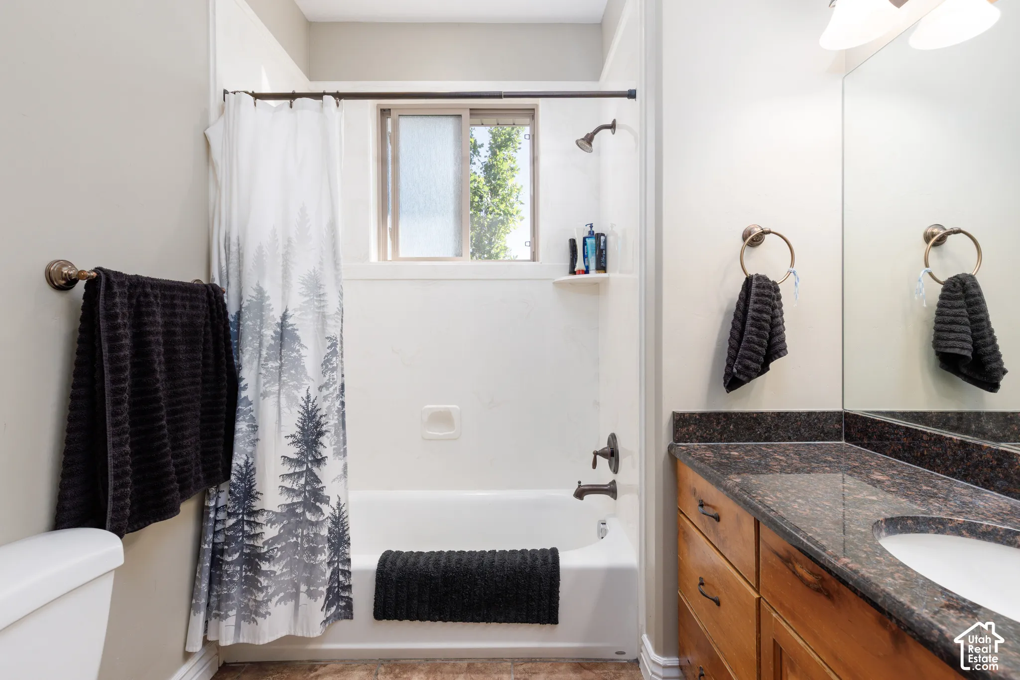 Bathtub with shower fixture, window with privacy glass, vanity with an integrated sink, dark speckled countertop, and wood-finish cabinetry