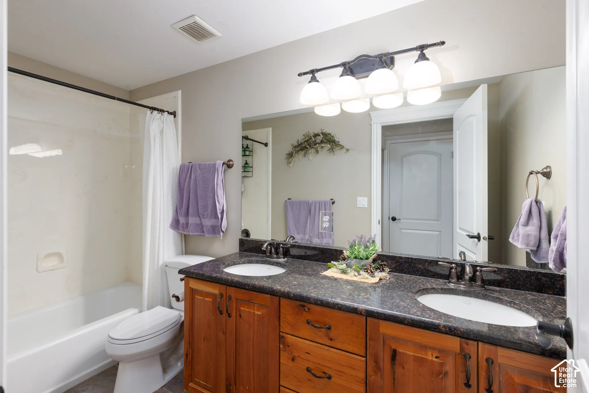 Dual vanity with dark stone countertop, undermount sinks, and wood-finish cabinetry