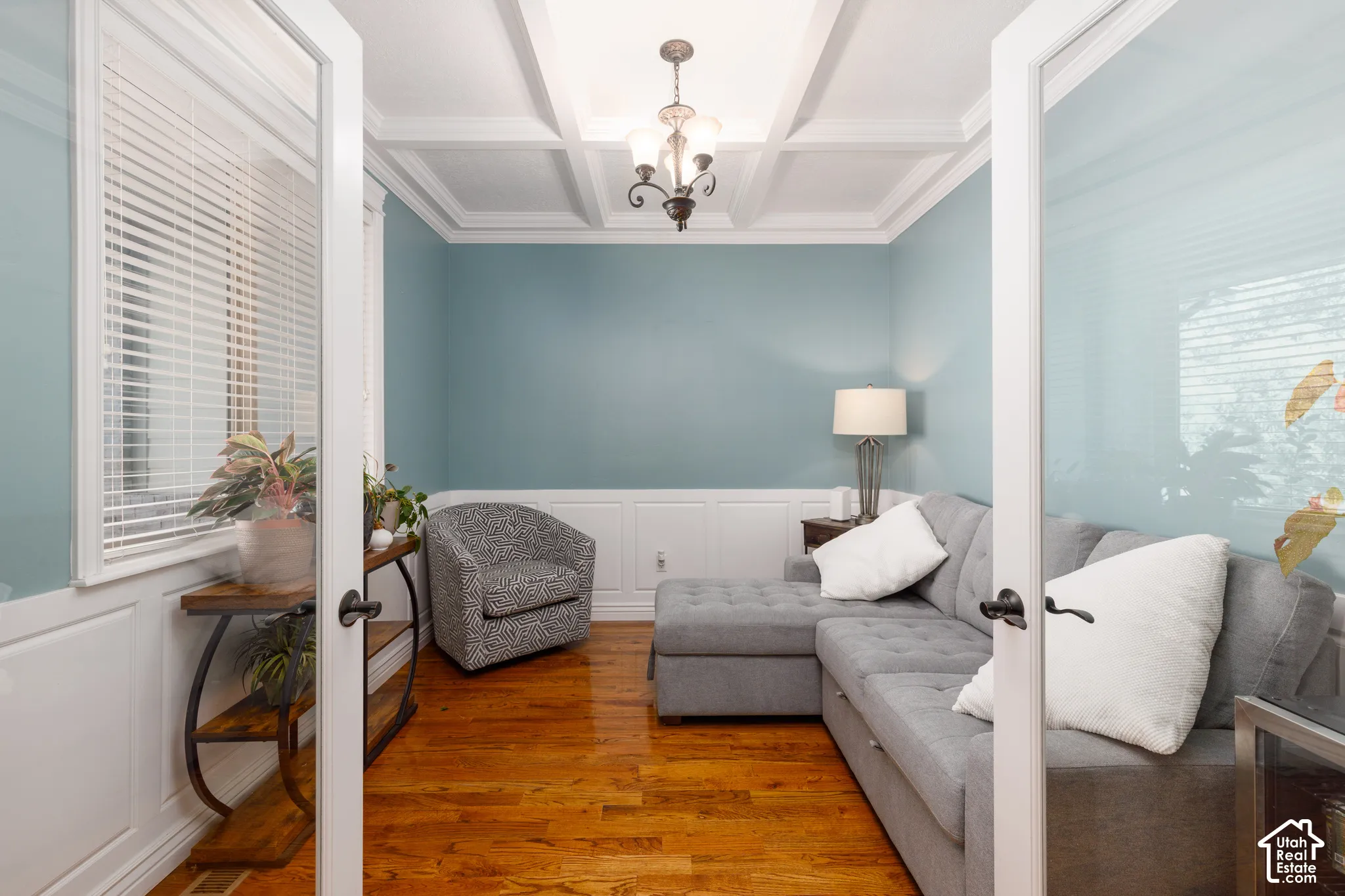 French doors opening to a room featuring wood-finish flooring, white coffered ceiling, and white wainscoting