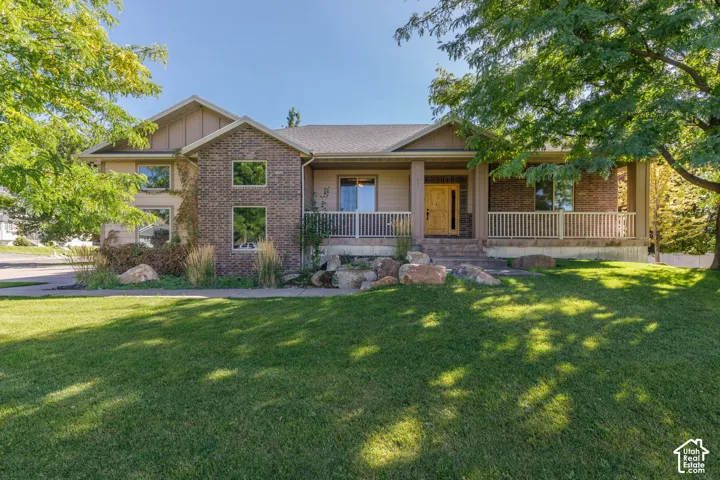 Expansive green lawn with mature trees, a brick and siding exterior, and a covered front porch with railing