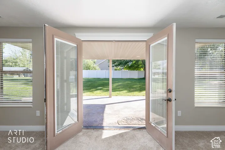 French doors opening to a covered concrete patio and a fenced backyard with a manicured lawn
