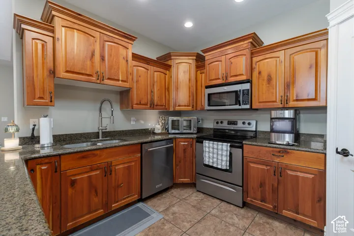 Wood cabinetry with crown molding, stainless steel appliances, granite countertops, tile flooring, and recessed lighting