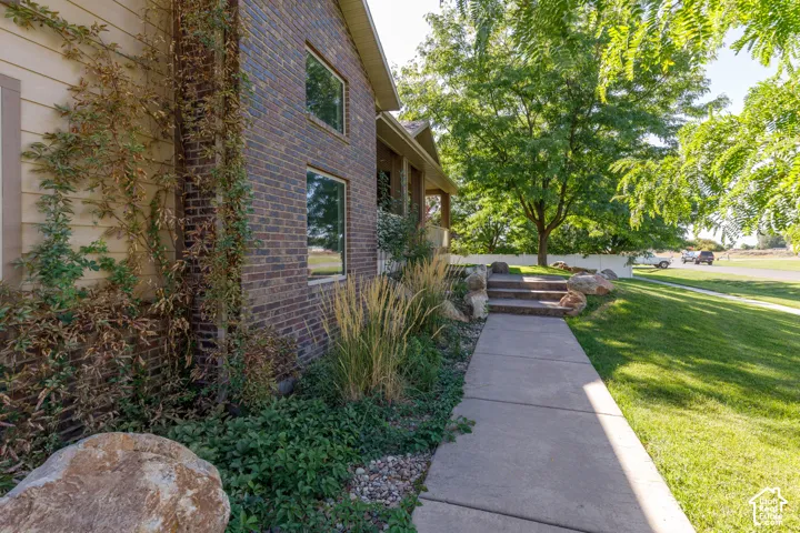 Brick exterior with climbing greenery, concrete walkway, stone-edged steps, and mature landscaping