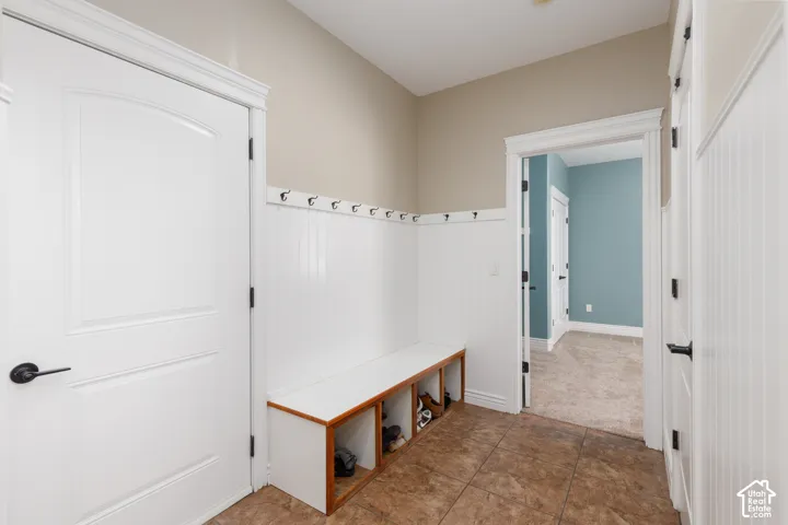 Entryway featuring tile flooring, wainscoting, an integrated bench with storage, and decorative wall hooks