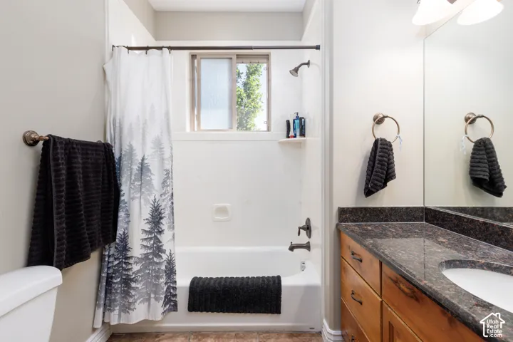 Bathtub with shower fixture, window with privacy glass, vanity with an integrated sink, dark speckled countertop, and wood-finish cabinetry