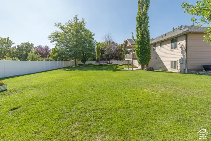 Expansive lawn area with a white privacy fence, mature trees, and a covered upper-level deck