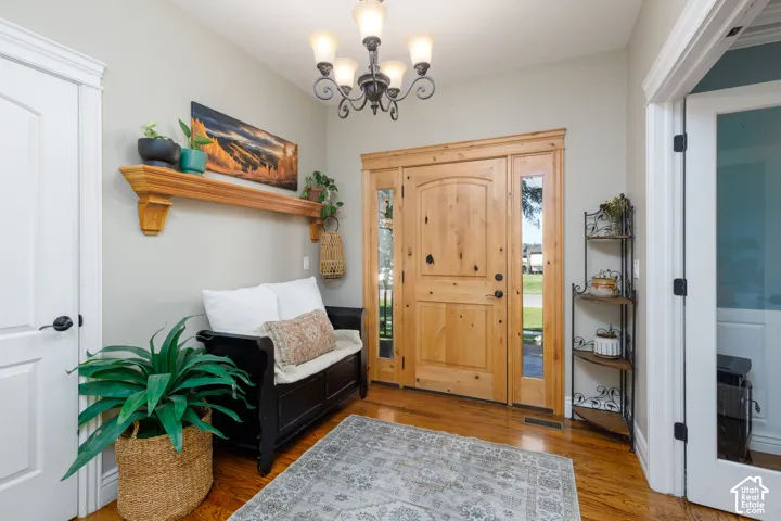 Hardwood flooring, natural wood-finish entry door with sidelights, decorative wall shelf, and chandelier with alabaster-style shades