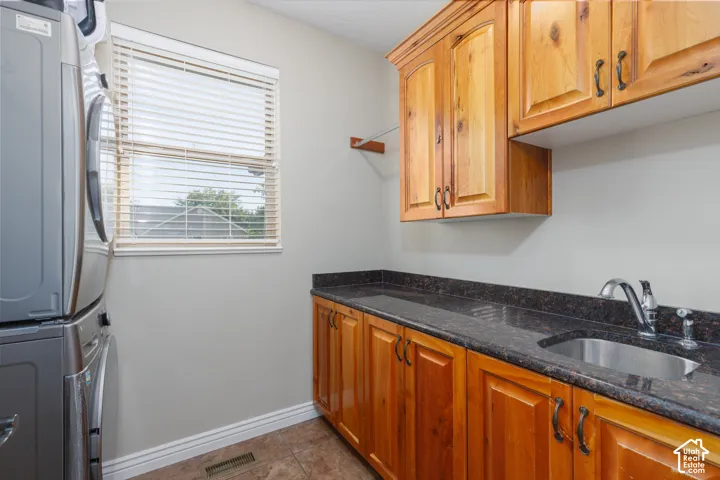 Laundry room featuring wood cabinetry, stone-finish countertop, and a stainless steel sink