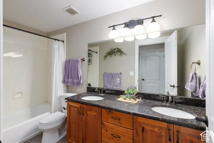 Dual vanity with dark stone countertop, undermount sinks, and wood-finish cabinetry