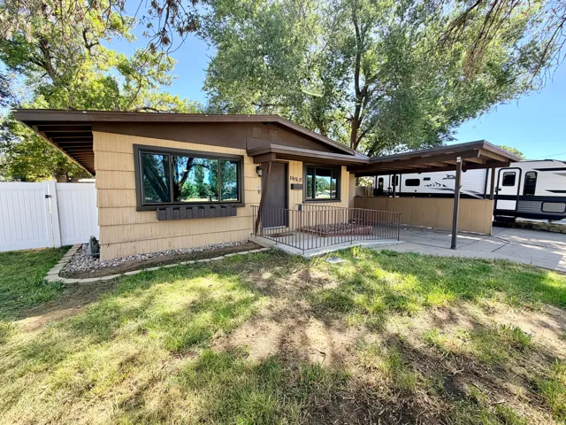Shingle-style siding exterior with dark trim, covered carport, white privacy fencing, and concrete entryway
