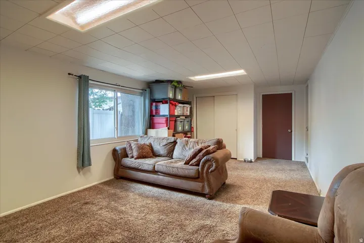 Plush carpet flooring, white walls, drop ceiling with integrated lighting, sliding door closet, and a single window
