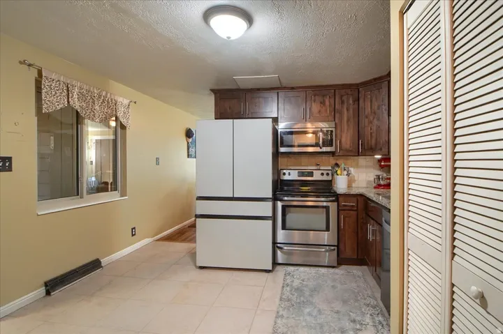 Kitchen featuring wood cabinetry, stainless steel appliances, a tile backsplash, and stone countertops
