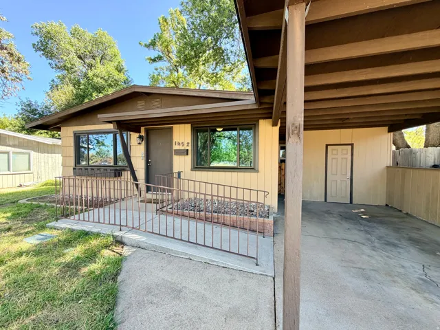 Front entrance with a ramp and metal railing, covered carport, exterior storage door, and a light-colored façade