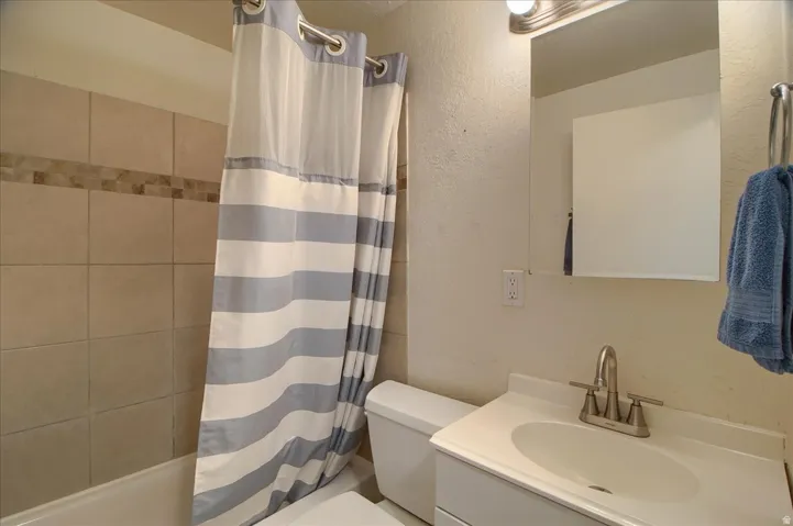 Bathroom featuring a bathtub, tiled shower surround with decorative accent band, vanity with integrated sink, brushed nickel faucet, and mirrored medicine cabinet