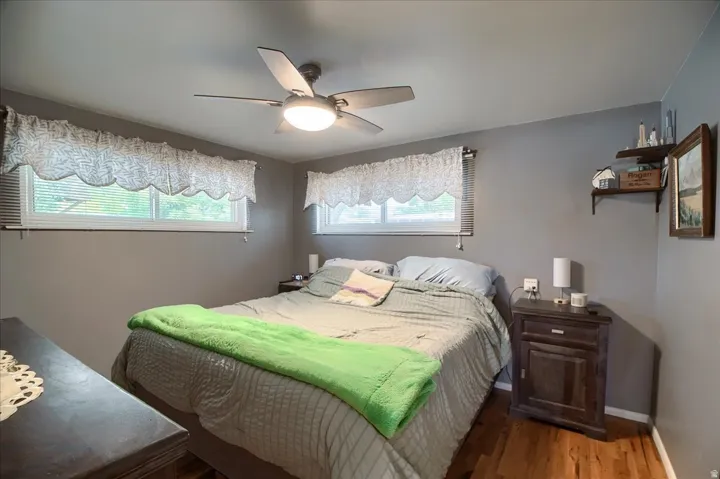 Hardwood-style flooring, ceiling fan with integrated lighting, two windows, and built-in shelving