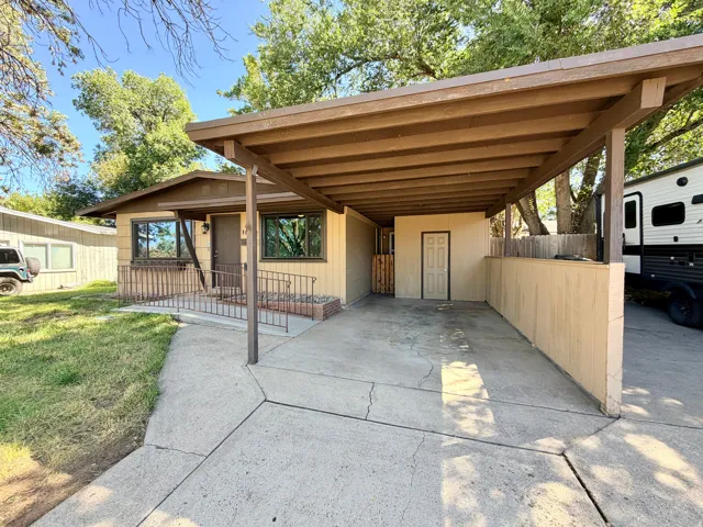 Covered carport, concrete driveway, front entry with metal railing, exterior storage room, and fenced side yard