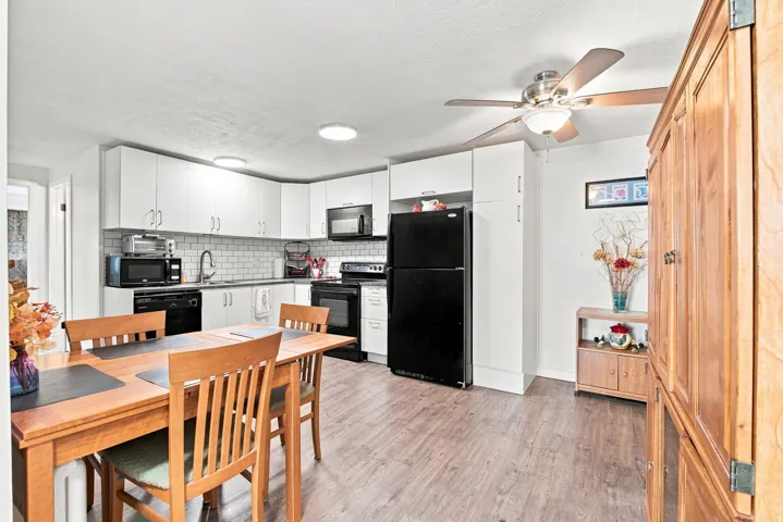 Kitchen with white cabinetry, subway tile backsplash, black appliances, and vinyl flooring
