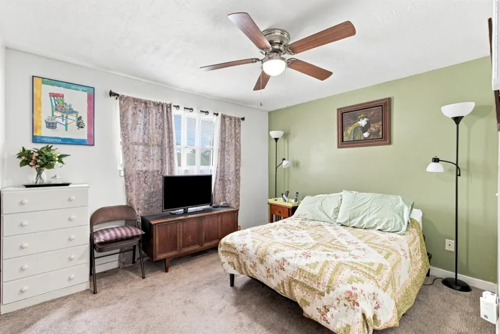 Ceiling fan with integrated lighting, light-colored carpeting, window with curtain rods, light green accent wall, and white trim throughout
