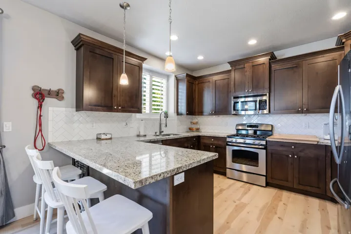 U-shaped kitchen with dark wood cabinetry, light granite countertops, stainless steel appliances, and wood-finish flooring