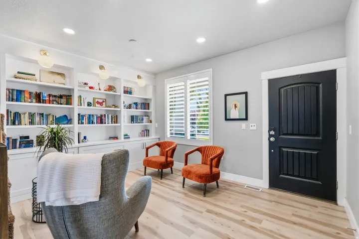 Built-in shelving with integrated lighting, wood-finish flooring, white window shutters, black paneled door, and recessed ceiling lights