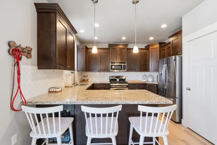 Gourmet kitchen featuring dark wood cabinetry, granite countertops, stainless steel appliances, and pendant lighting over a generous island with seating for three