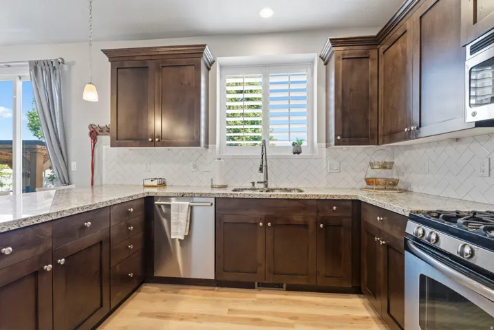 Wood-finish flooring, stainless steel appliances, white herringbone tile backsplash, and light-toned countertops