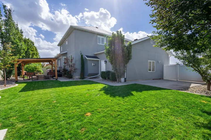 Expansive lawn area, mature trees, wood pergola, paved patio, and a privacy fence