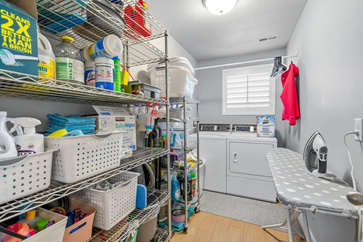 Laundry area featuring a window with white shutters, dual laundry appliances, and overhead lighting