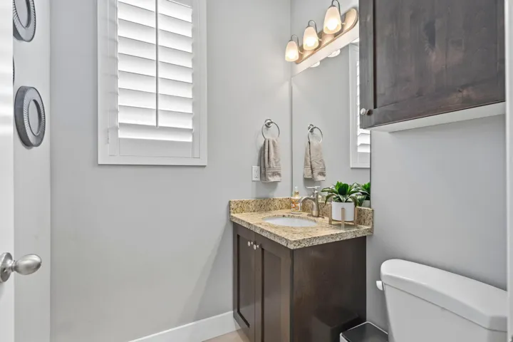 White plantation shutters on a window, dark wood-finish vanity with a granite-style countertop, undermount sink, and brushed nickel faucet