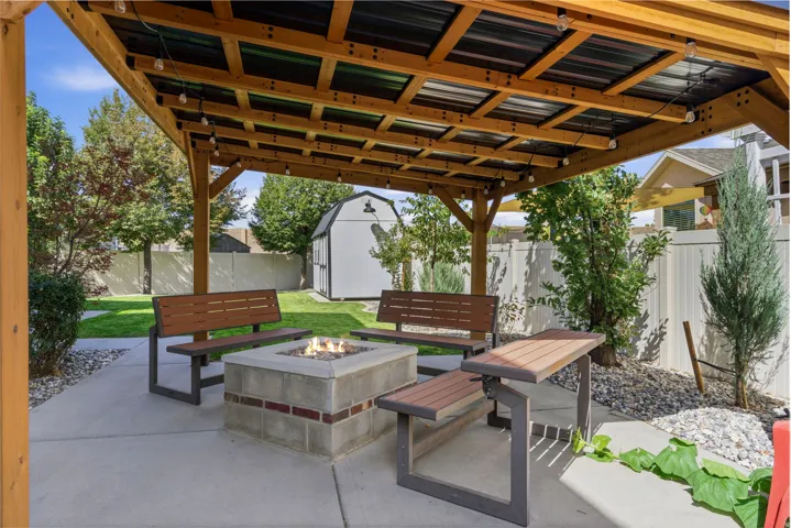 Covered patio with a built-in fire pit featuring a concrete and brick-finish base, string lighting, and direct access to a manicured lawn