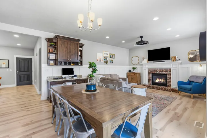 Wood-finish flooring throughout, integrated built-in desk, built-in cabinetry, brick-surround fireplace with a white mantel, and wainscoting