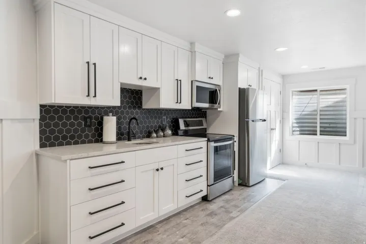 White cabinetry, stainless steel appliances, black hexagonal tile backsplash, light-toned countertop, and recessed lighting